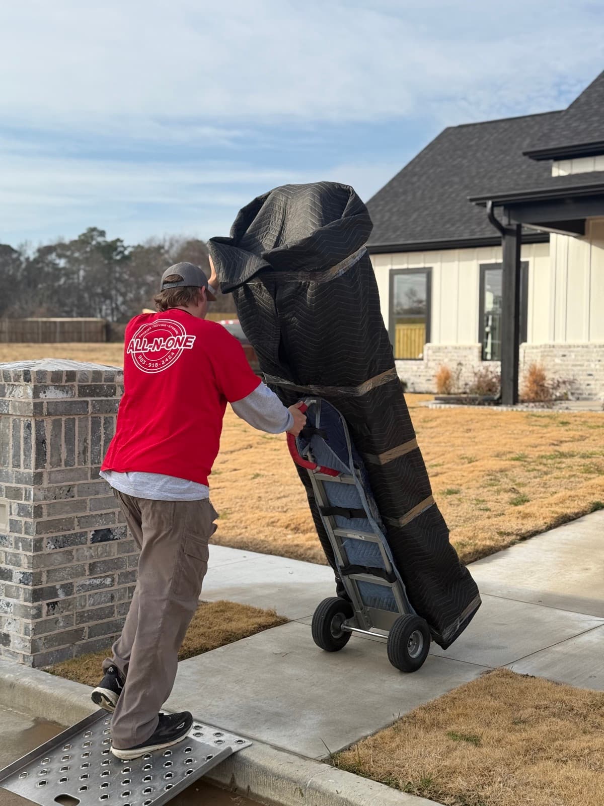 All-N-One Moving crew member moving a wrapped mattress on a hand truck at a customer's home